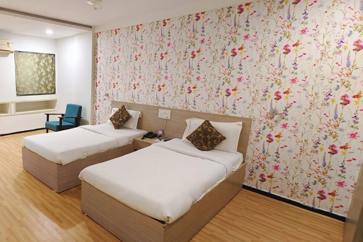 A hotel room with two beds, a small seating area, and floral wallpaper.
