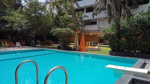 En swimmingpool med metallstegar, omgiven av planterade växter och utemöbler.