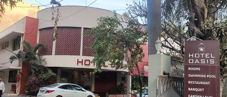 A hotel entrance with a sign listing amenities like rooms, swimming pool, restaurant, banquet, garden lawn, and bakery.