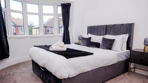 Een netjes opgemaakt bed met een donker hoofdbord, wit beddengoed en een zwarte plaid.