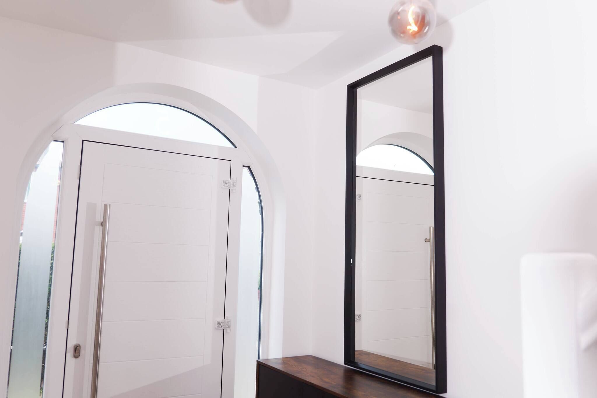 A modern bathroom with a white tiled wall, a wooden vanity, and a large mirror.