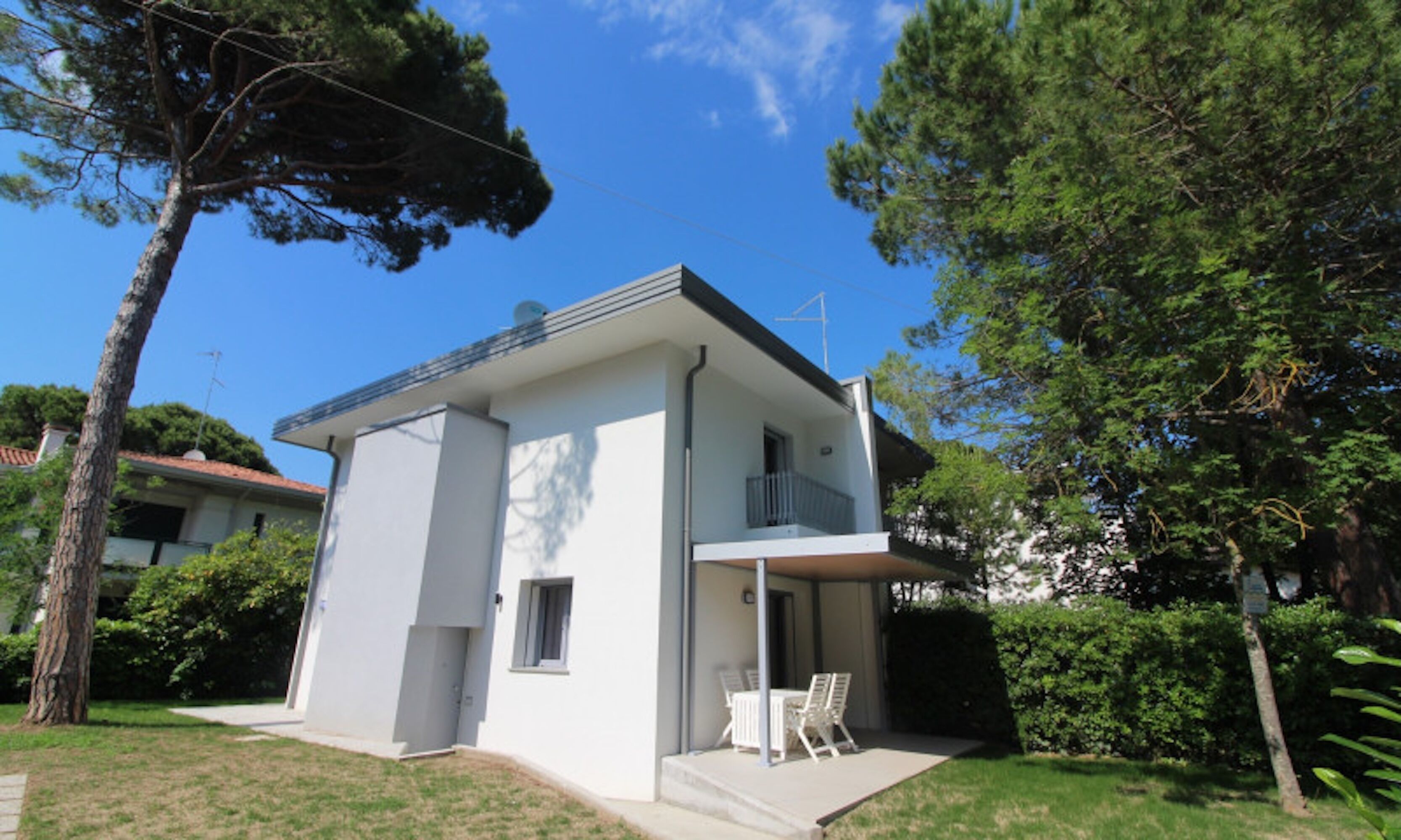 A modern two-story house with a balcony, surrounded by trees and a clear sky.