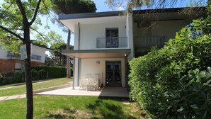 A modern two-story house with a covered patio, a small balcony, and a well-maintained lawn. - Modern Villa With a Fenced Garden (Lignano Sabbiadoro)