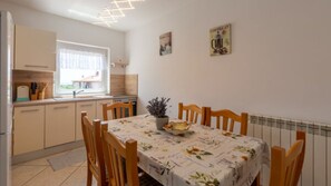 Ein Essbereich mit einem für vier Personen gedeckten Tisch, umgeben von Holzstühlen. Auf dem Tisch steht ein Blumentopf, und es sind zwei Wandposter angebracht.