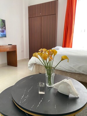 A hotel room with a bed, a wooden wardrobe, a round table with a vase of flowers, and a television on the wall. - Enkang View Palace Apartments (Nairobi)