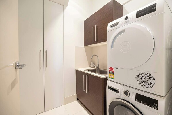 A compact laundry room with a Bosch washing machine, a sink, and wooden cabinets. - Bella Vista | Pool, spa & bay views (Mornington)