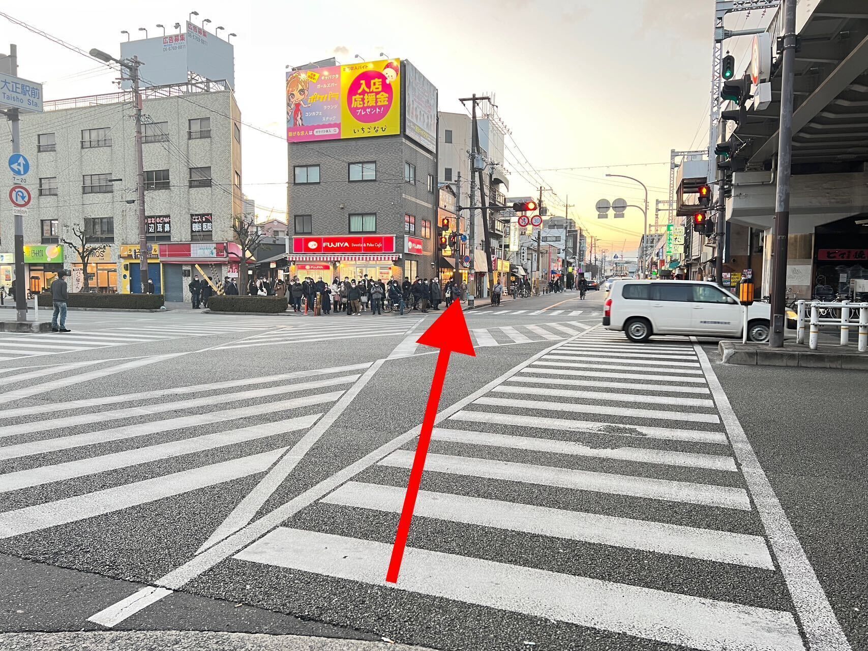 A crosswalk with a red arrow pointing forward, surrounded by buildings and a white van.