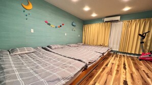 Una habitación con dos camas, suelo de madera, ventilador de techo y una ventana con cortinas.