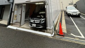 Un edificio de varios pisos con acceso a un garaje, un coche aparcado y una calle visible.