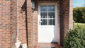 Ein Backsteinhaus mit weißer Tür, einer kleinen Veranda und einem Metalllüfter.