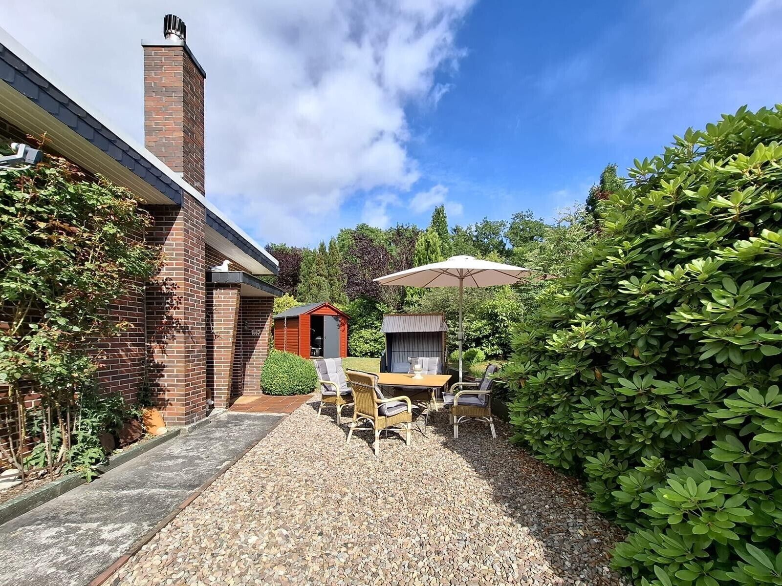 A patio with a table and chairs, a small shed, and a brick building with a chimney.