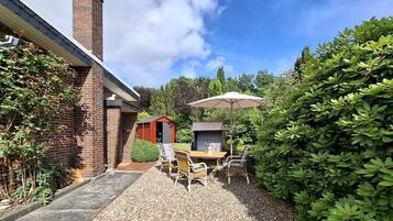 A patio with a table and chairs, a small shed, and a brick building with a chimney.