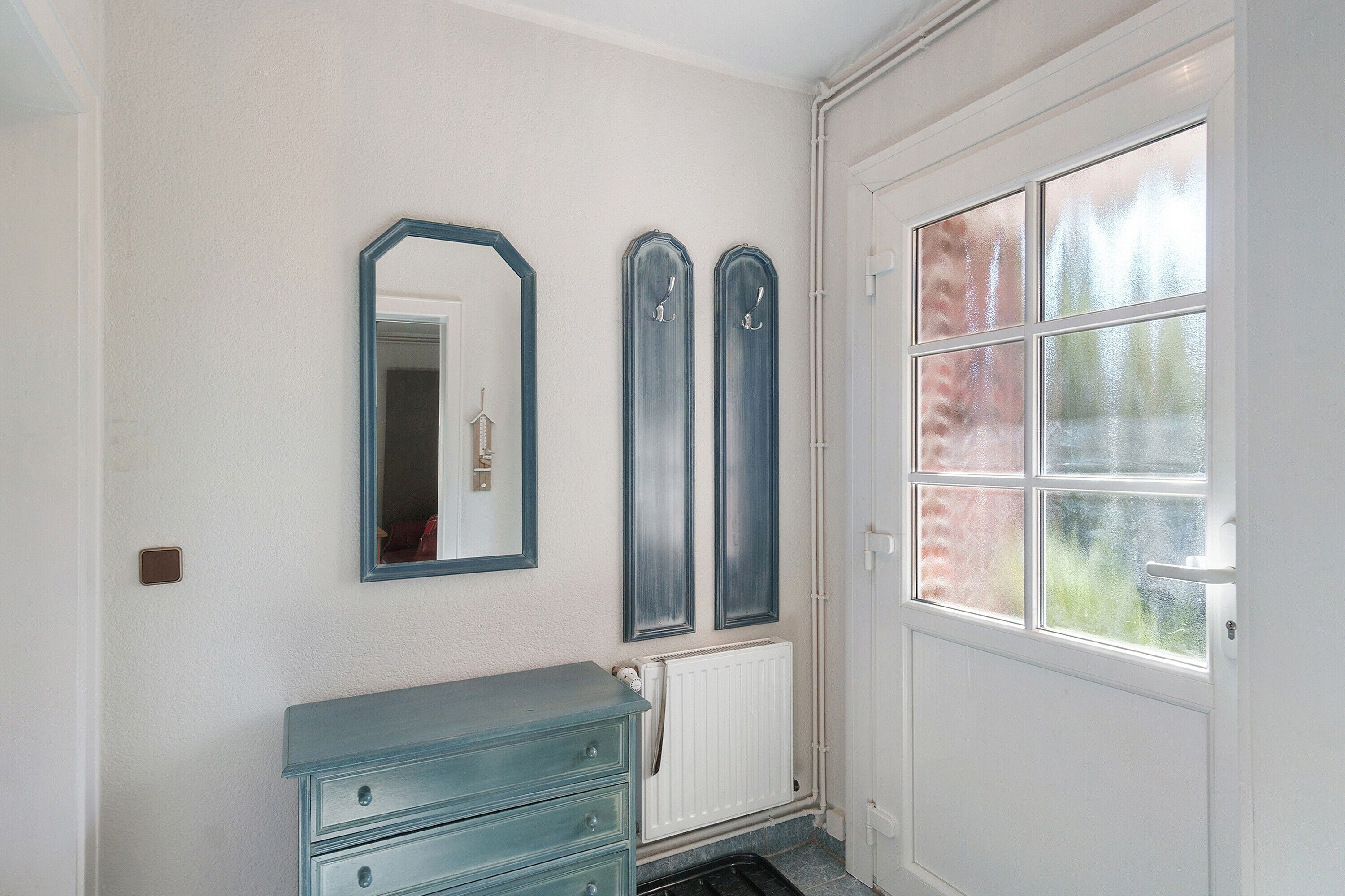 Une salle de bain avec un radiateur blanc, une commode bleue et une grande fenêtre donnant sur les arbres.
