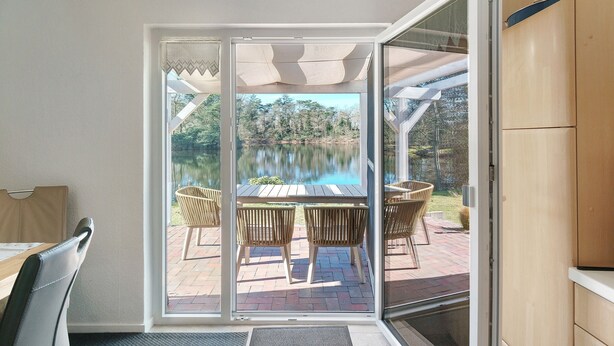Ein Zimmer mit einer Schiebetür zu einer Terrasse im Freien mit Tisch und Stühlen, einem Pool und einer Holzvertäfelung.