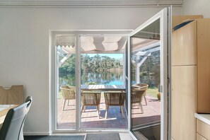 A room with a sliding glass door leading to an outdoor patio with a table and chairs, a pool, and a wooden cabinet. - Idyllic lakeside cottage (Bockhorn)