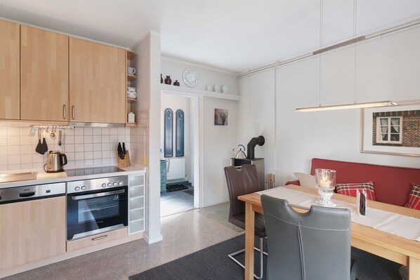 A modern kitchen with wooden cabinets, a built-in oven, and a dining area with a table and chairs. - Idyllic lakeside cottage (Bockhorn)
