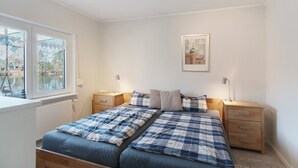 Ein Schlafzimmer mit zwei Betten, einem Fenster mit Blick, einem Nachttisch mit Lampe und einem gerahmten Bild an der Wand.