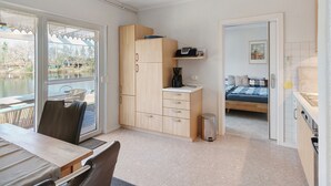 Ein kleines Zimmer mit Bett, Küchenzeile und Seeblick durch ein Fenster.