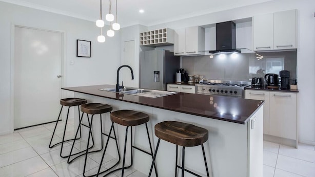 A modern kitchen with a central island, bar stools, a gas stove, and a built-in oven. - Tennela Haven North Lakes (North Lakes)