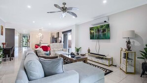 A modern living room with a grey sofa, red chair, and a ceiling fan. - Tennela Haven North Lakes (North Lakes)