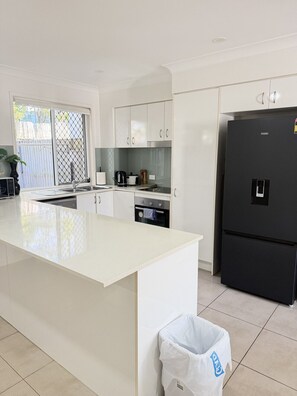 A modern kitchen with a large island, white cabinetry, a black refrigerator, and a window with a view. - Syldah Stay Mango Hills (Mango Hill)