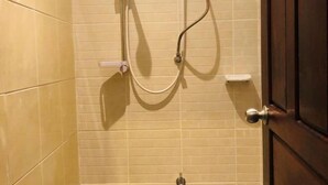 A bathroom with beige tiled walls, a shower with a handheld showerhead, and a door with a silver handle. - Hide and Seek Hostel Vientiane (Thai Embassy) (Vientiane)