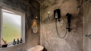 A bathroom with a white sink, a handheld showerhead, a wall-mounted speaker, and a window with a view of a green field. - Chill Tangalle (Tangalle)