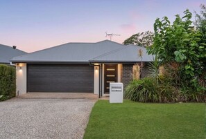 Une maison moderne avec une porte de garage sombre, une allée en gravier et une pelouse bien entretenue.