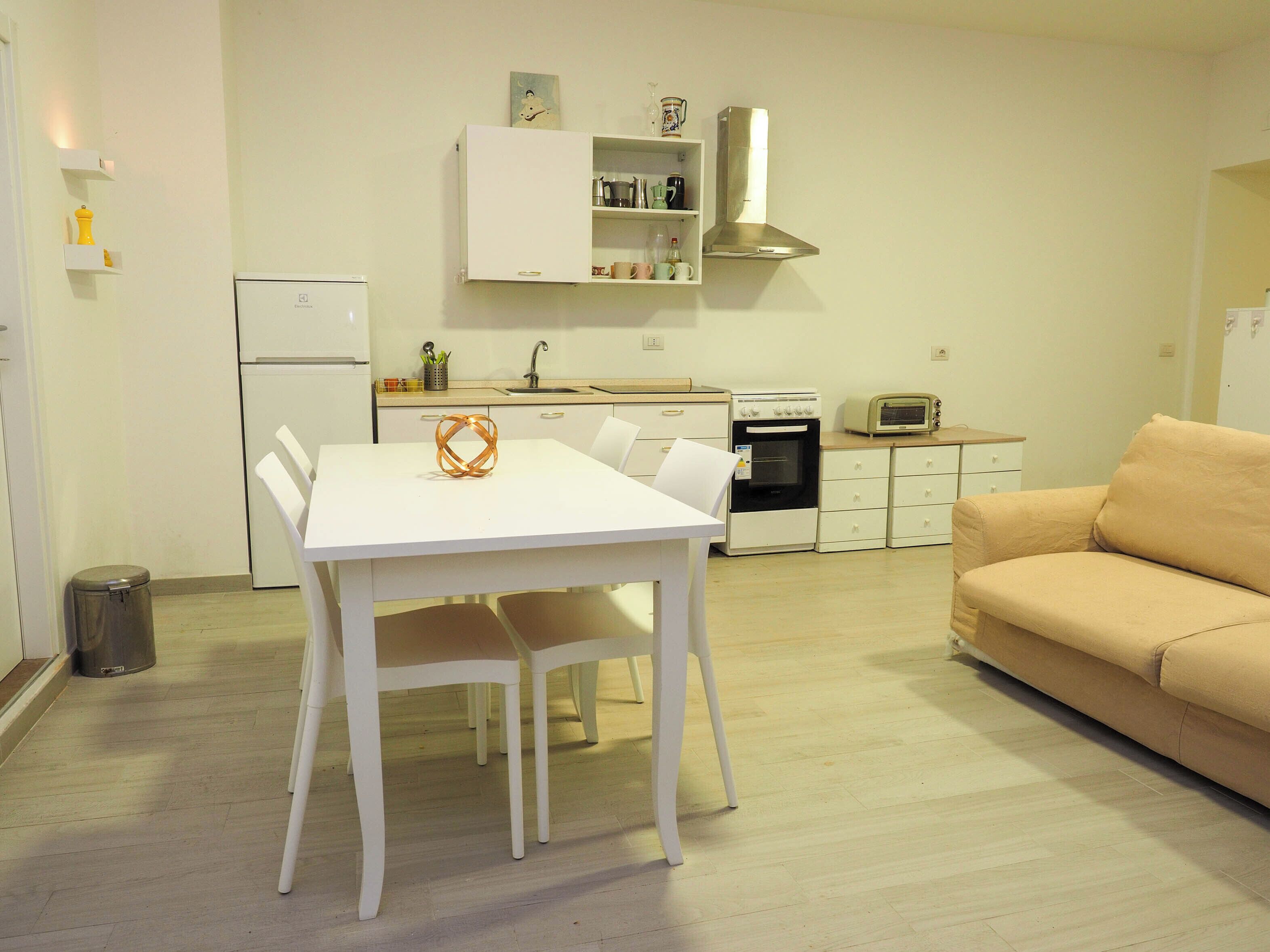 A compact kitchen with a white table, a beige sofa, and a trash bin.