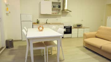 Een kleine keuken met een witte tafel, een beige bank en een prullenbak.