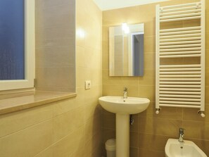 A bathroom with beige tiles, a pedestal sink, a mirror, a towel rack, and a bidet.