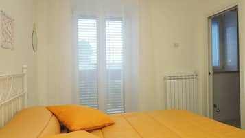 A bedroom with a bed, two pillows, a radiator, and a window with blinds.