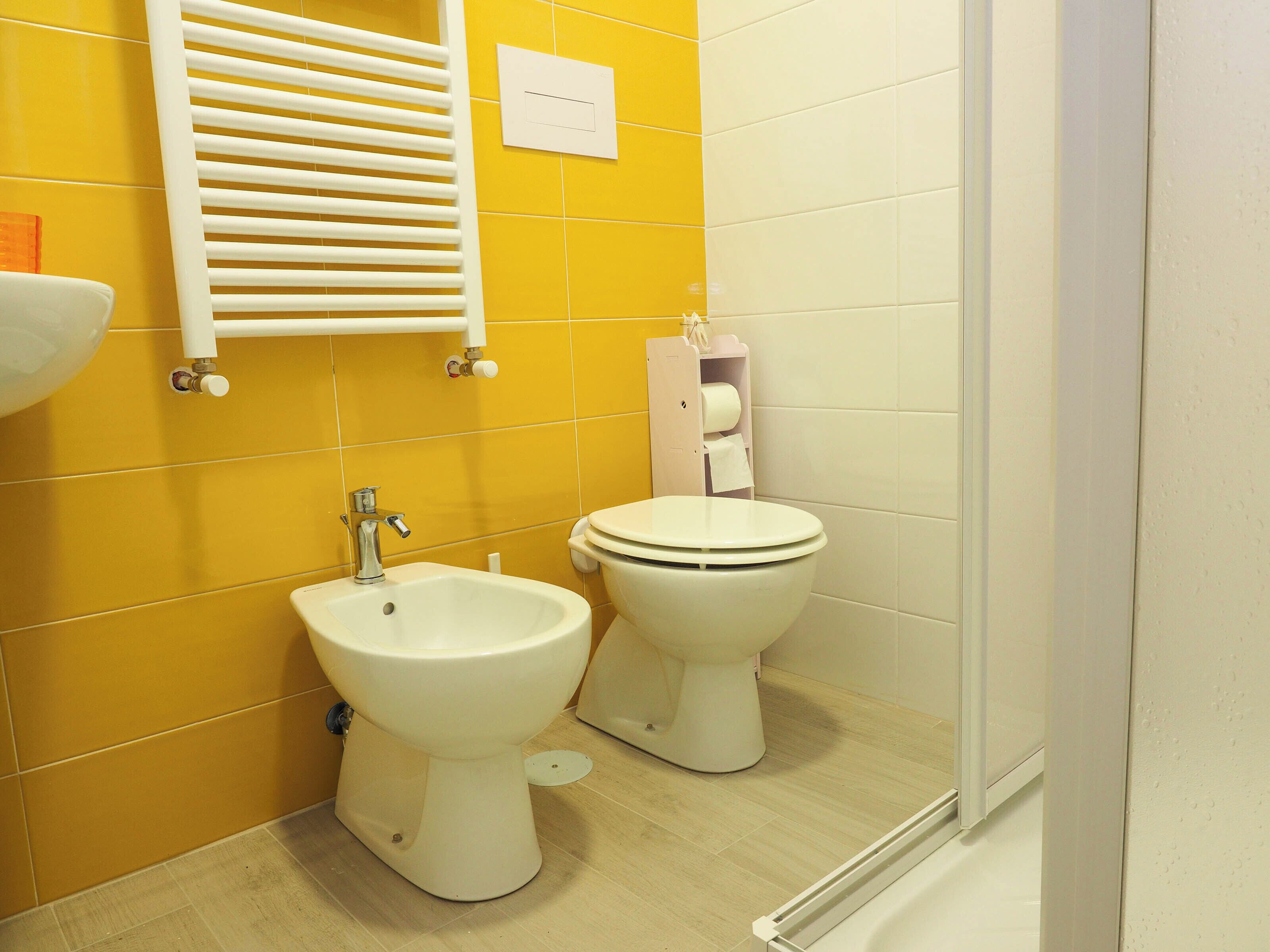 A bathroom with yellow walls, a white sink, a bidet, a toilet, and a towel rack.
