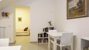 En moderne stue med en sofa, et spisebord med stole, en bogreol og et billede på væggen.
