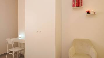 Een minimalistisch ingerichte kamer met een wit bureau, een witte stoel en een klein plankje met boeken en kaarsen.