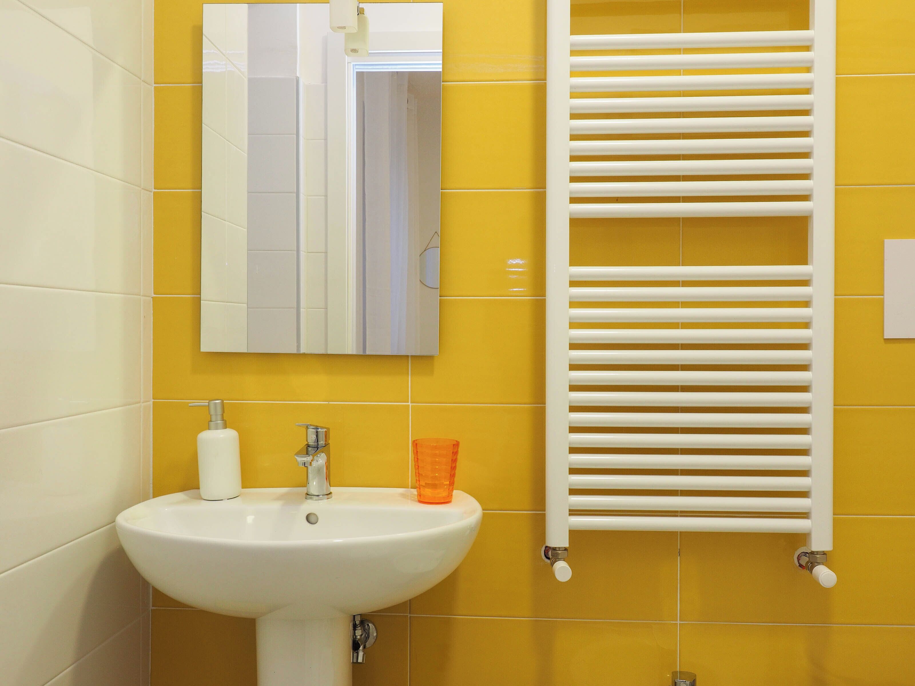 A bathroom with a white sink, a mirror, and a white towel rack against yellow walls.