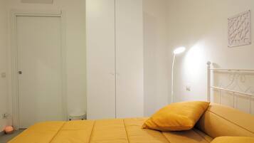 A bedroom with a bed, a wardrobe, a bedside lamp, and a small stool.