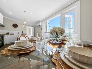 Una cocina moderna con una mesa de comedor de vidrio, armarios blancos y un ventanal que deja entrar luz natural.