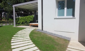 A modern house with a covered patio, a stone pathway, and a bench. - Modern Villa 250mt From the Beach (Lignano Sabbiadoro)