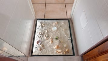 A tiled floor with a square opening, possibly a door or window, with scattered seashells.