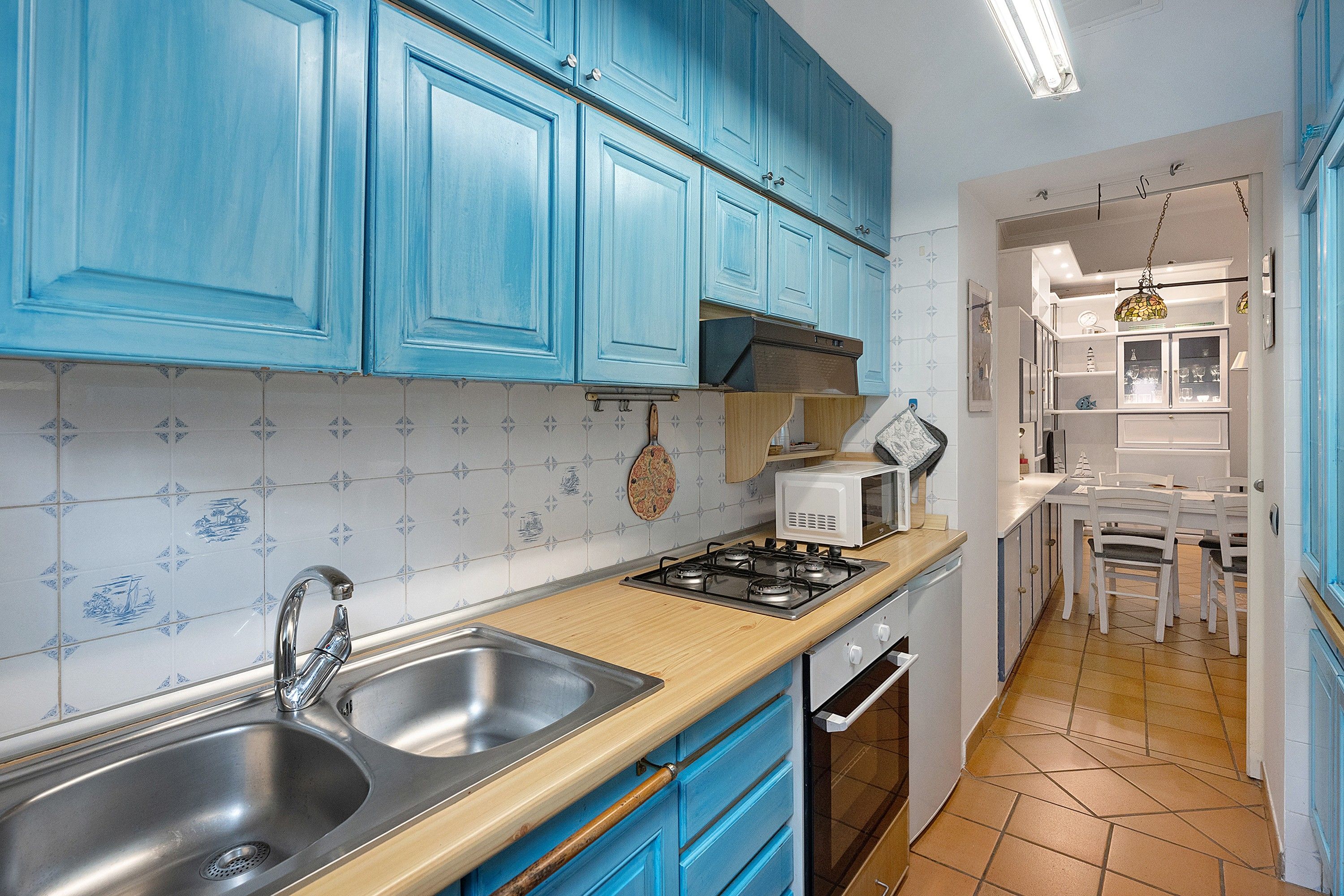 A kitchen with blue cabinets, a stainless steel sink, a stove, and a microwave.