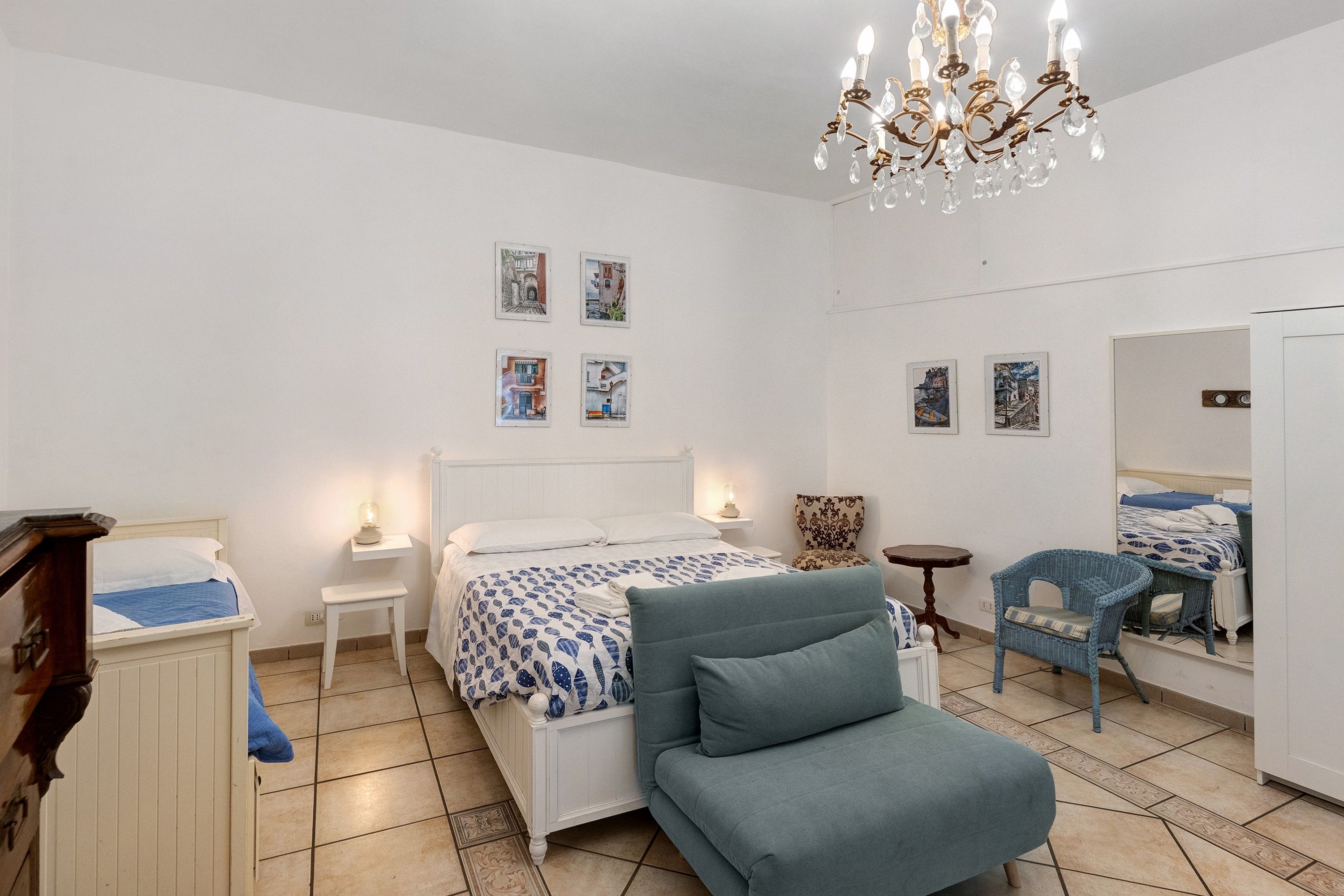 A bedroom with a bed, a chair, a dresser, a nightstand, and a chandelier.