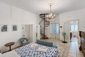 Un dormitorio con cama, una silla, un tocador, un ventilador y una escalera.
