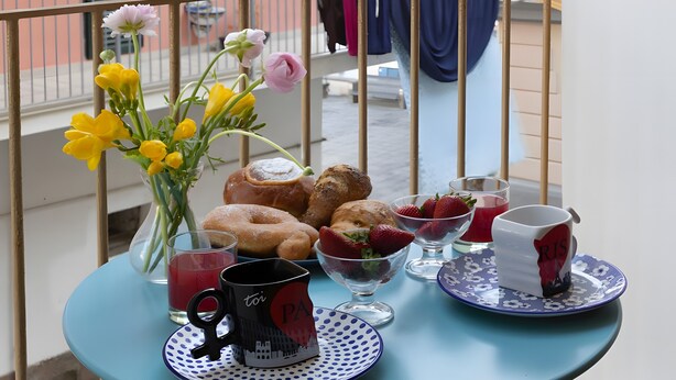 Ett bord med bakverk, en vas med blommor och en mugg på en balkong.