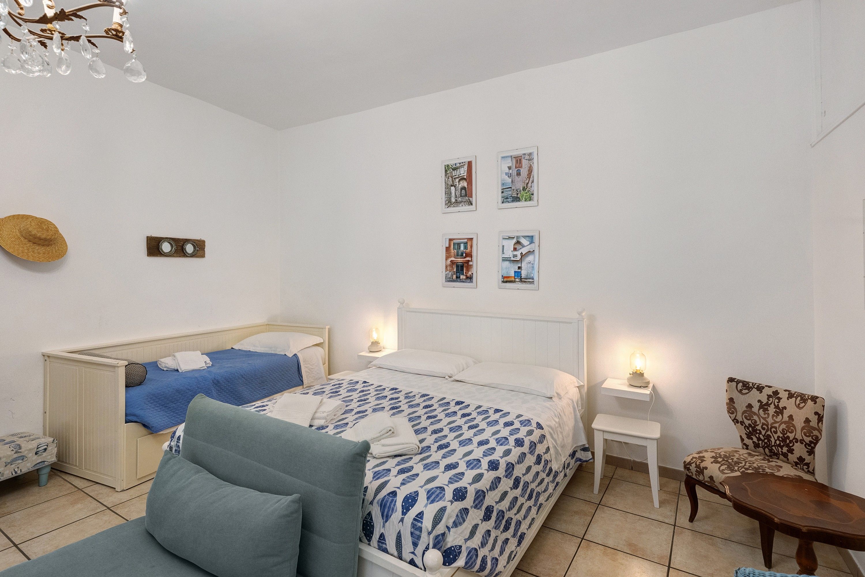 A bedroom with a bed, two bedside tables, a chair, a small table, and a wall-mounted shelf.