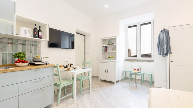 A modern kitchen with a dining area, white cabinetry, a flat-screen TV, and a window with a view. - Holiday Home 'Domus Mediterranea' with Wi-Fi and Air Conditioning (Sorrento)