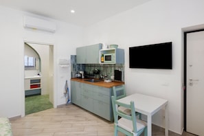 A compact kitchen with a microwave, sink, and cabinets, a small dining table with a chair, and a door leading to another room. - Holiday Home 'Domus Mediterranea' with Wi-Fi and Air Conditioning (Sorrento)