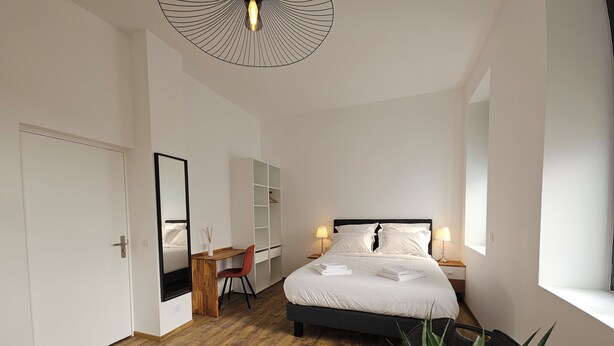 A bedroom with a bed, desk, chair, and a large mirror. - La Bastide Foch – Premium Appart’Hotel City Center (Salon-de-Provence)