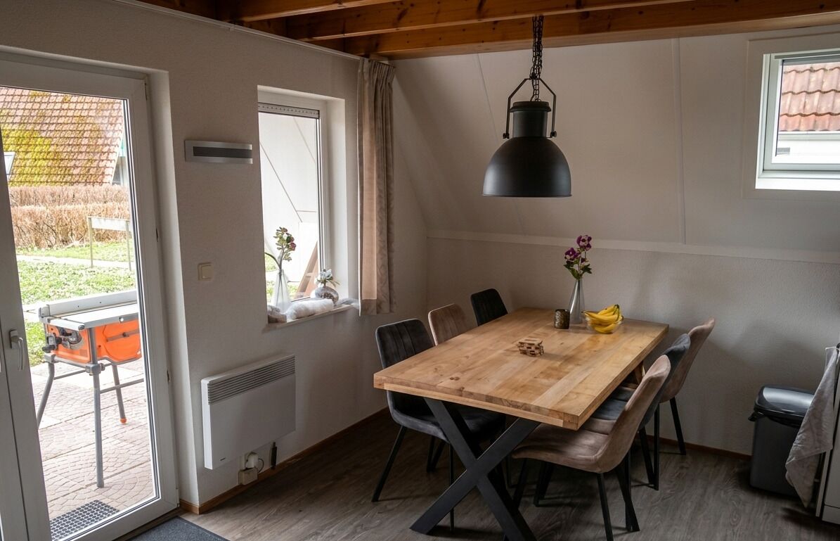 Een eethoek met een houten tafel, zwarte stoelen en een hangende lamp.