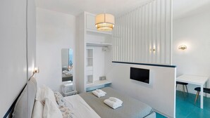 Una habitación de hotel con cama, escritorio, televisor, armario y espejo de baño.